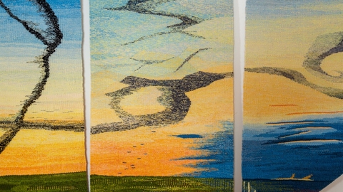 Vividly coloured tapestry showing flocks of bird flying close together and making patterns in the sky.