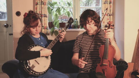 Christina is playing a banjo and Alex is holding a fiddle and bow