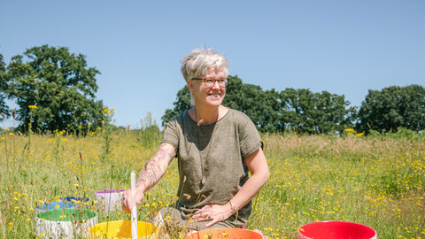 A lady sitting in a summer meadow with 4 brightly-coloured round crystal bowls
