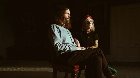 Musicians Samantha Whates and MG Boulter are seated facing sideways -on, in a dark room