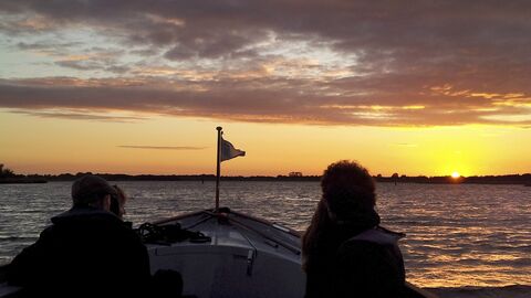 Two people sail a boat across Hickling Broad as the sun comes up
