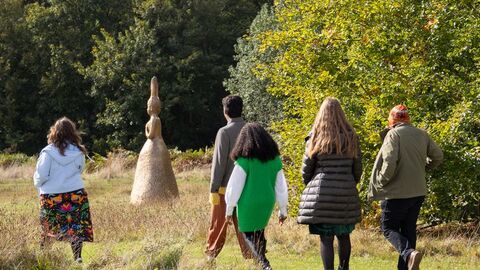 A group of people walking across a grassy area with a sculpture and trees behind them