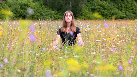 A woman seated in a yoga position in a wildflower meadow