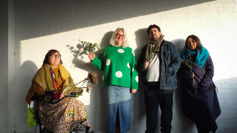 Four people facing the camera holding foliage, three are standing and one is seated in a wheelchair