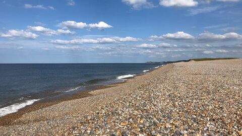 A photo of the shingles beach at Cley, with waves lapping on the shore and white clouds in a blue sky