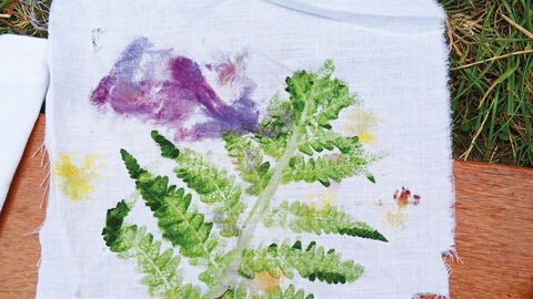A piece of white material with a green fern leaf and purple flower print on it