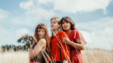 Murmurations band members wearing brightly coloured clothing and standing in a meadow of yellow grass