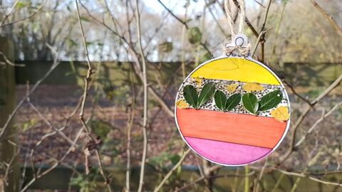 A pink, yellow and green Christmas bauble made out of paper and foraged leaves