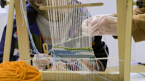 Two ladies working to create a woven tapestry on a wooden loom
