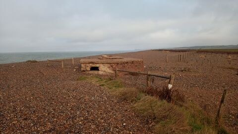 A WW2 military building on a shingle beach, with the sea in the distance