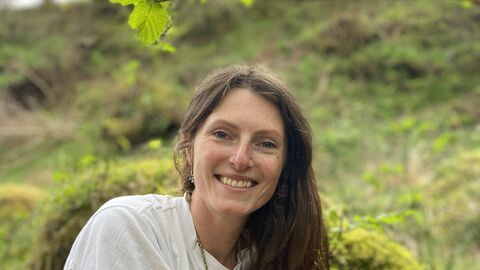 Lucy is wearing a white t shirt and is sitting in woodland, smiling at the camera 