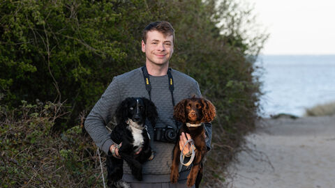 Alfie is standing on a track with his back to the sea. He is holding a spaniel under each arm.