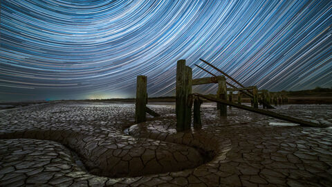 A special effect nighttime photo of wooden posts with parched dry ground and a swirling blue sky