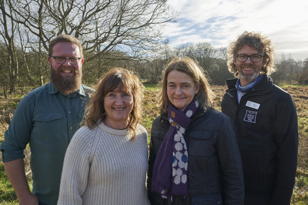 Three Aviva team members and NWT's Eliot Lyne stand smiling at the camera at Sweet Briar Marshes on a sunny day.