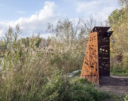 Concept art featuring a brown, metal bird viewing structure, looking out across trees and bushes on Sweet Briar Marshes