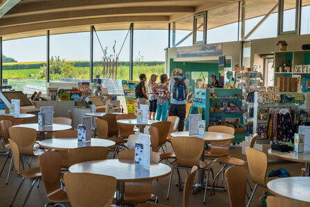 NWT Cley Visitor Centre, showing tables and chairs, welcome desk and views through large glass walls onto the nature reserve