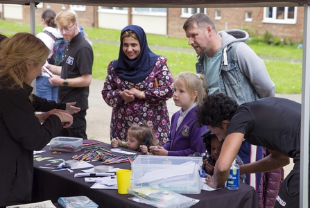 Families chatting to NWT staff at a stall on Lefroy Estate. Some children and making use of the colouring pencils and paper on the stall.