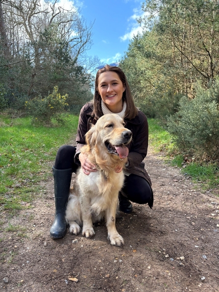 Bailey kneeling down posing with her golden retriever dog outdoors.