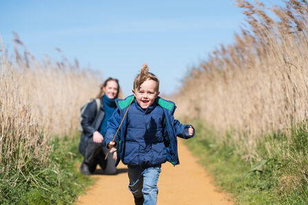A young boy happily runs towards the camera brandishing a stalk of reed