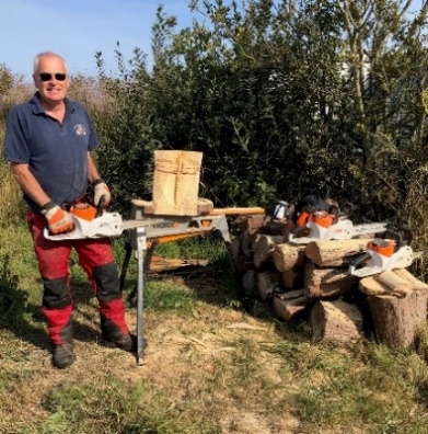Chainsaw artist volunteer, Andy Usher, grinning with his tools and creations outside at Hickling. 