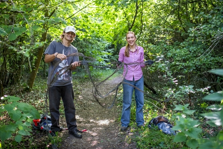 Two teen members of the youth forum, a boy and girl, holding up a large twig they are clearing. 