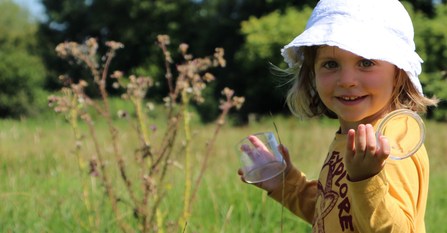 A child smiles and holds a bug pot in a sunny meadow