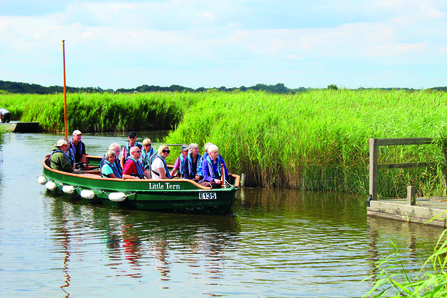 A small boat full of smiling people in life jacket son Hickling Broad on a sunny day. 