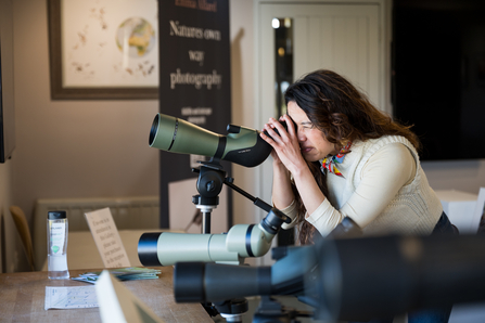 A woman is looking through a Cley Spey scope at a visitor centre.