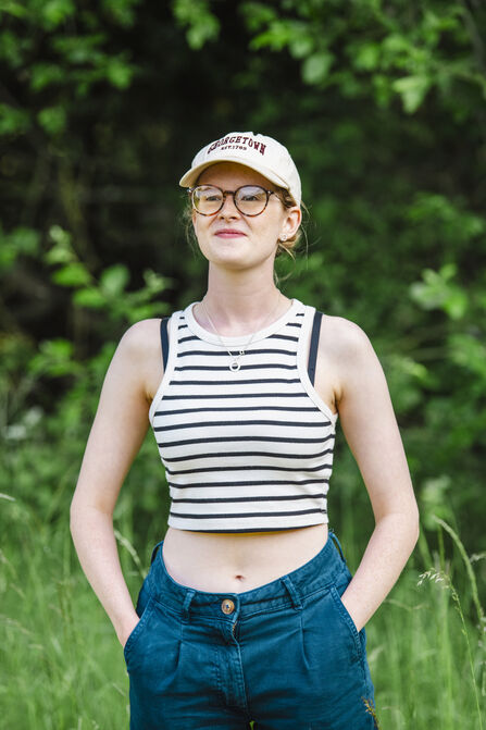 A teenage girl wearing a beige cap, brown glasses and a black and white striped crop top is smiling at the camera.