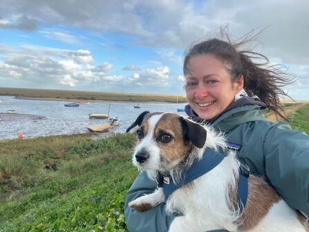 A woman outside on a windy day on the coast with her little dog. 