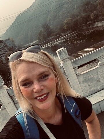 A woman with blonde hair smiling whilst on holiday. 