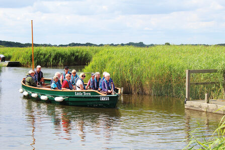 A small boat full of smiling people in life jackets on Hickling Broad on a sunny day 