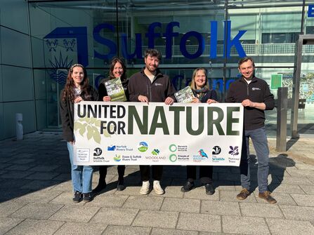 Smiling Suffolk Wildlife Trust staff posing outside Suffolk County Council holding up a banner that says, 'united for nature'.