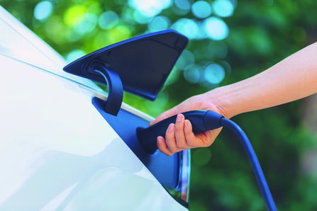 Close up of a hand plugging in an electric vehicle to be charged.