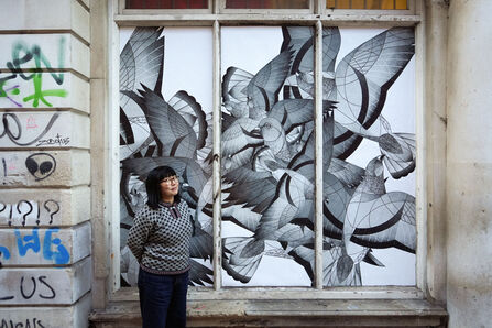 Artist Alice Lee stands by a mural of pigeons