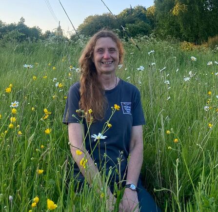 Smiling woman with curly hair crouched in a blooming meadow, smiling. 