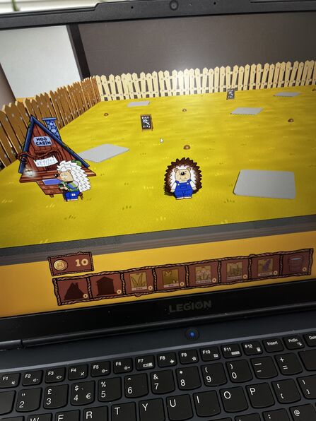 A photo of an animated video game on a laptop screen. The game features hedgehogs on a patch of grass, surrounded by a wooden fence.