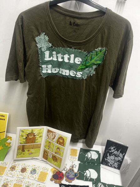 A display featuring a green t-shirt with 'little homes' written on it, along with some leaves. There are also nature booklets and images on a table in front of it, all with bright graphics.