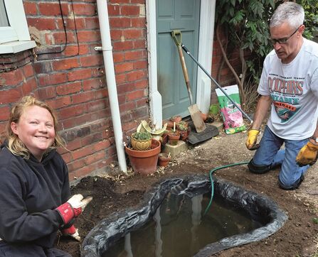 Two people filling a newly dug out pond using a water butt