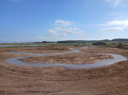 a view over a flat area of mud with a small stream in it