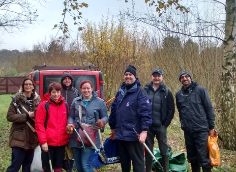 A group of people wearing winter clothes smile at the camera as they hold litter pickers