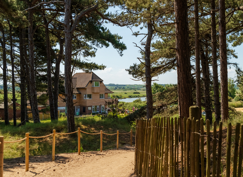 Holme visitor centre between the trees with a wooden picket fence and sandy path. 