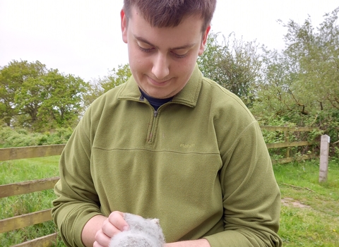 A young man in a green fleece holds a baby tawny owl