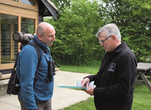 A member of staff showing a visitor directions on the reserve outside Hickling visitor centre