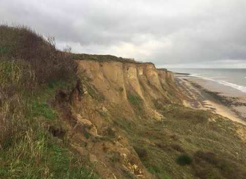 Sandy, grassy cliffs sweep down to a beach on a grey day
