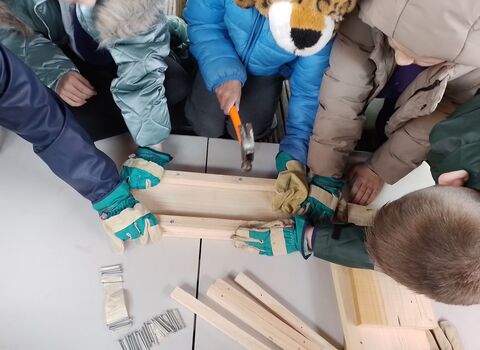 A group of children pictured from above using hammers to build a nest box