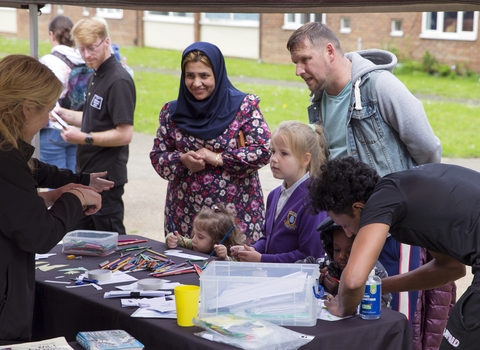 Families chatting to NWT staff at a stall on Lefroy Estate. Some children and making use of the colouring pencils and paper on the stall.
