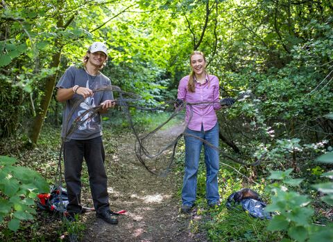 Two teen members of the youth forum, a boy and girl, holding up a large twig they are clearing. 
