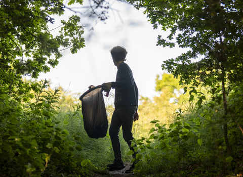 A young boy picking up litter in a woodland. 