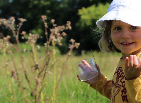 A child smiles and holds a bug pot in a sunny meadow